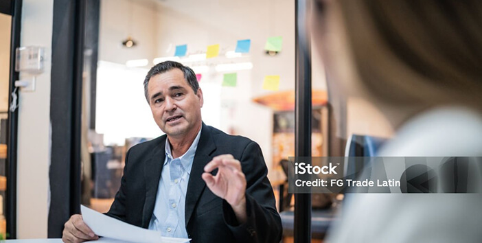 A business man in a suit gesturing to someone facing away from camera
