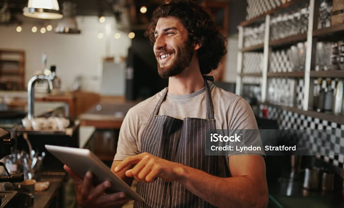 A hospitality worker smiling as he uses his tablet device